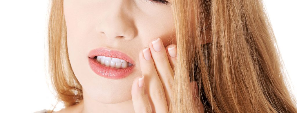 Stock image of a woman feeling pain eyes closed by holding her left side of mouth with left hand